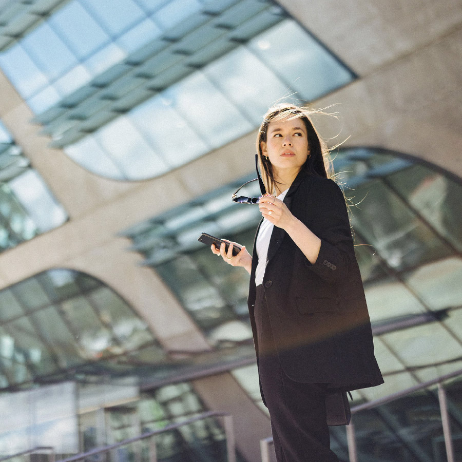 Business woman with cellphone and sunglasses standing in front of a building