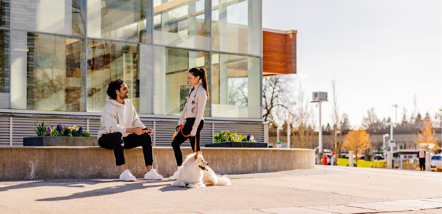 Athletic looking man and woman with a dog talking in front of a building